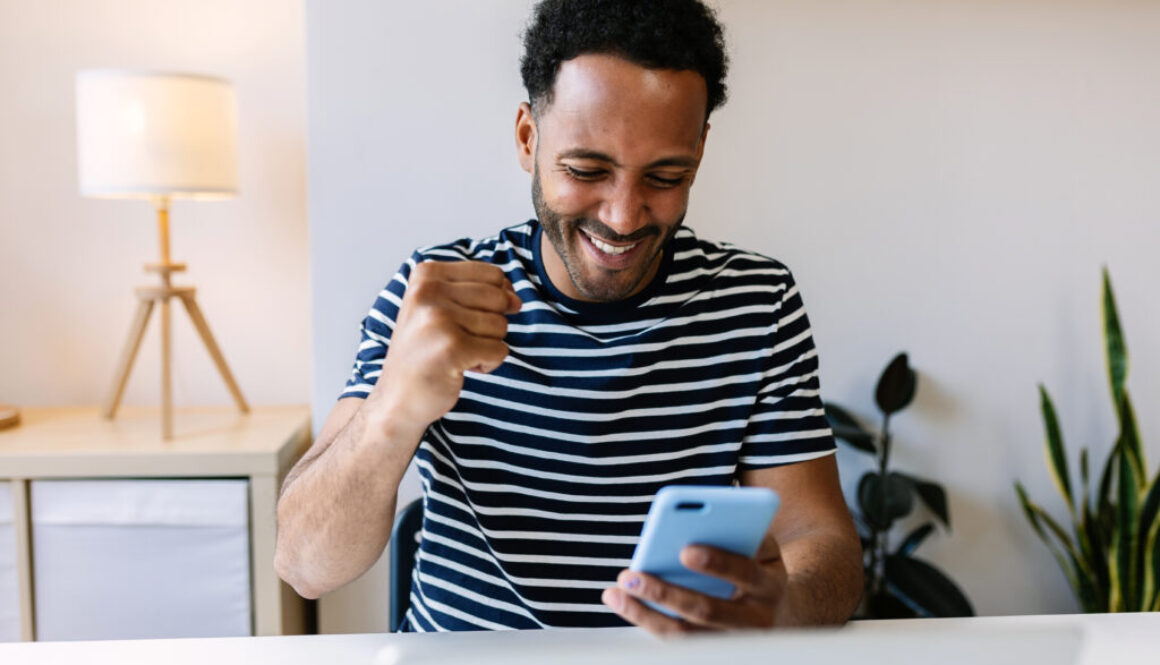 Excited young african american man winning on internet lottery betting online on smartphone app. Millennial guy celebrating victory enjoying success sports bet on cellphone.