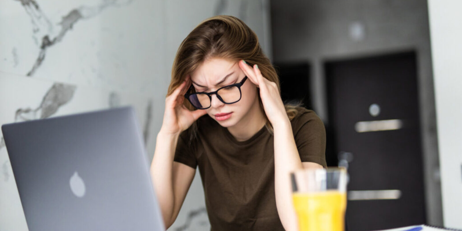 Mobile Office at home. Exhausted tired woman working using on laptop holding head in hand sitting in kitchen at home. Young girl studying or working indoors. Freelance business quarantine concept
