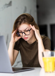 Mobile Office at home. Exhausted tired woman working using on laptop holding head in hand sitting in kitchen at home. Young girl studying or working indoors. Freelance business quarantine concept