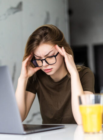 Mobile Office at home. Exhausted tired woman working using on laptop holding head in hand sitting in kitchen at home. Young girl studying or working indoors. Freelance business quarantine concept