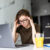 Mobile Office at home. Exhausted tired woman working using on laptop holding head in hand sitting in kitchen at home. Young girl studying or working indoors. Freelance business quarantine concept